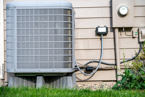 Outdoor residential air conditioner on an elevated pad. Electrical utility hookups on building exterior. 