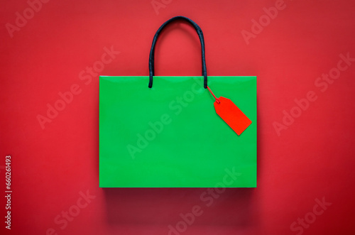 Green shopping paper bag with red blank price tag on red background for Black Friday shopping sale concept.
