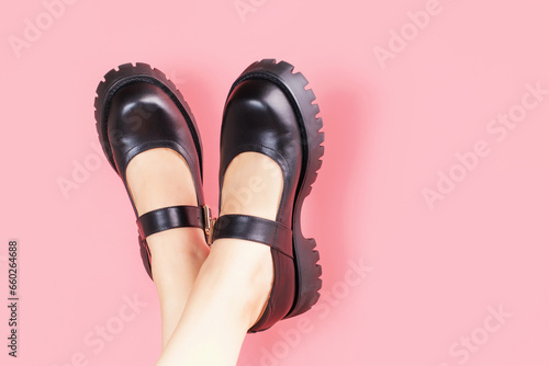 Female legs in black leather shoes upside down on pink background with copy space.