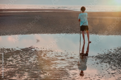 A teenage boy plays in a pool of water left was the tide goes out, stopping to look at the sunrise