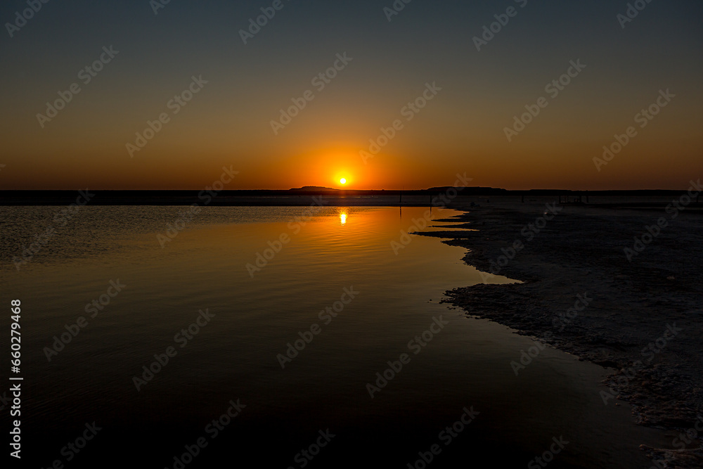 Sunset or sunrise on salt lake Baskunchak (Russia). Bright sun in a cloudless sky, calm brine in the saline. Morning or evening in summer, autumn or spring.
