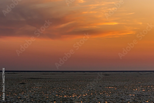 Sunset or sunrise on salt lake Elton (Russia) with mirror or reflection of low Cumulostratus or Stratocumulus clouds in the brine at golden hour. Evening or morning. Volrograd district.