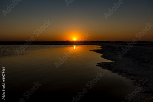 Sunset or sunrise on salt lake Baskunchak (Russia). Bright sun in a cloudless sky, calm brine in the saline. Morning or evening in summer, autumn or spring.
