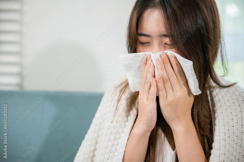 Sick female sitting under blanket on sofa and sneeze with tissue paper in living room, fever caught cold, Asian young woman she sick blowing nose sneezing in tissue at home, medicine healthcare Sick female sitting under blanket on sofa and sneeze with tissue paper in living room, fever caught cold, Asian young woman she sick blowing nose sneezing in tissue at home, medicine healthcare