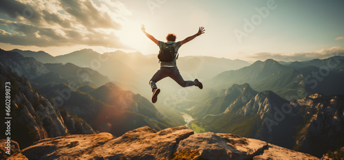 Happy man lifts his arms and jumps on the mountaintop - Successful hiker celebrates success on the cliff - Lifestyle concept and young man climbing on the forest trail photo