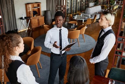 High angle portrait of restaurant manager talking to servers wearing classic uniforms during staff meeting in modern dining room photo