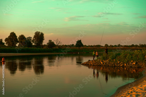 Beautiful river bank. the setting sun illuminates with warm rays a family that casts fishing rods on the shore. fishing. amazing landscape. the concept of a family vacation in nature. copy space