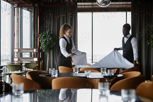 Tablou pe pânză Side view portrait of two elegant waiters setting tables in luxury restaurant an
