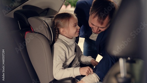 Cute little girl waits while father unlocks safety belt of child seat in car