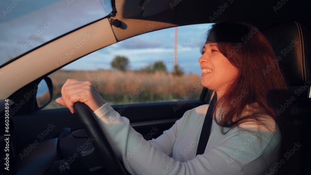 Young woman drives car holding steering wheel along rural road under cloudy sky