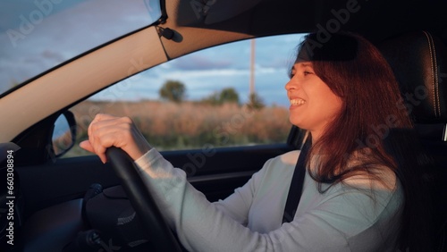 Young woman drives car holding steering wheel along rural road under cloudy sky © Валерий Зотьев