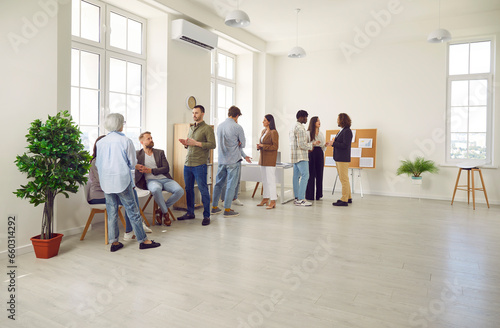 Full length photo of a group of business people men and women chatting after a meeting. Company employees team or group of staff talking with each other in the office during the break.