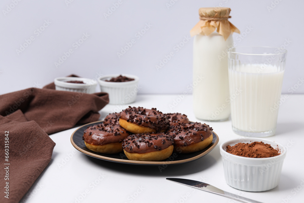 Chocolate donuts on plate, bottle and glass with milk and bowls on white background