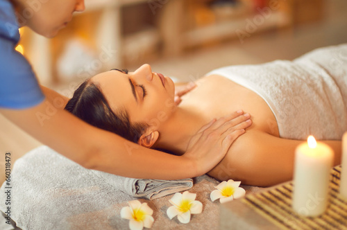 Portrait of pretty young brunette woman with closed eyes relaxing in spa salon getting massage. Therapist doing manipulative treatment on shoulders. Wellness and beauty day concept.