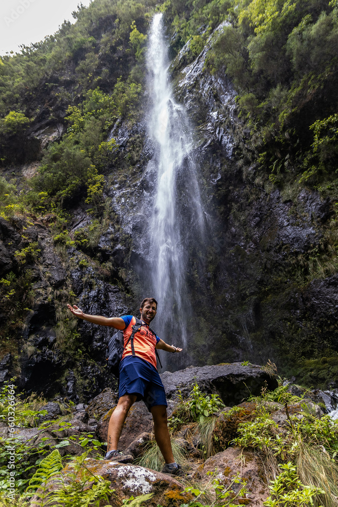 Person located at the foot of a waterfall with an excited face and opening his arms. Route that runs from the road between the levada of Caldeirão Verde and Caldeirão do Inferno