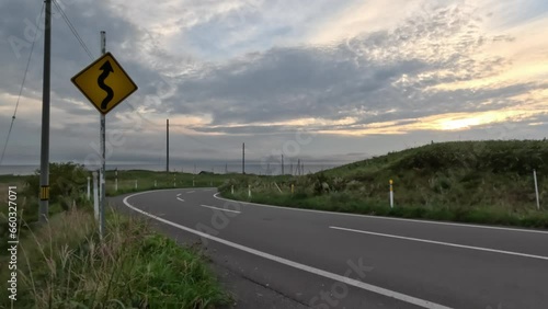 Curves ahead sign on open empty road in coastal landscape at sunset
