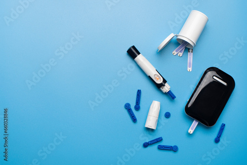 Diabetes awareness concept of glucose meter test strips and lancets on blue background flat lay