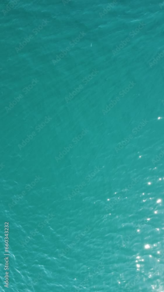 Vertical aerial view on sea water surface, camera flies over clear sea water. Sun glare. Abstract nautical summer ocean nature. Holiday, vacation and travel concept. Nobody. Vertical video Vertical aerial view on sea water surface, camera flies over clear sea water. Sun glare. Abstract nautical summer ocean nature. Holiday, vacation and travel concept. Nobody. Vertical video