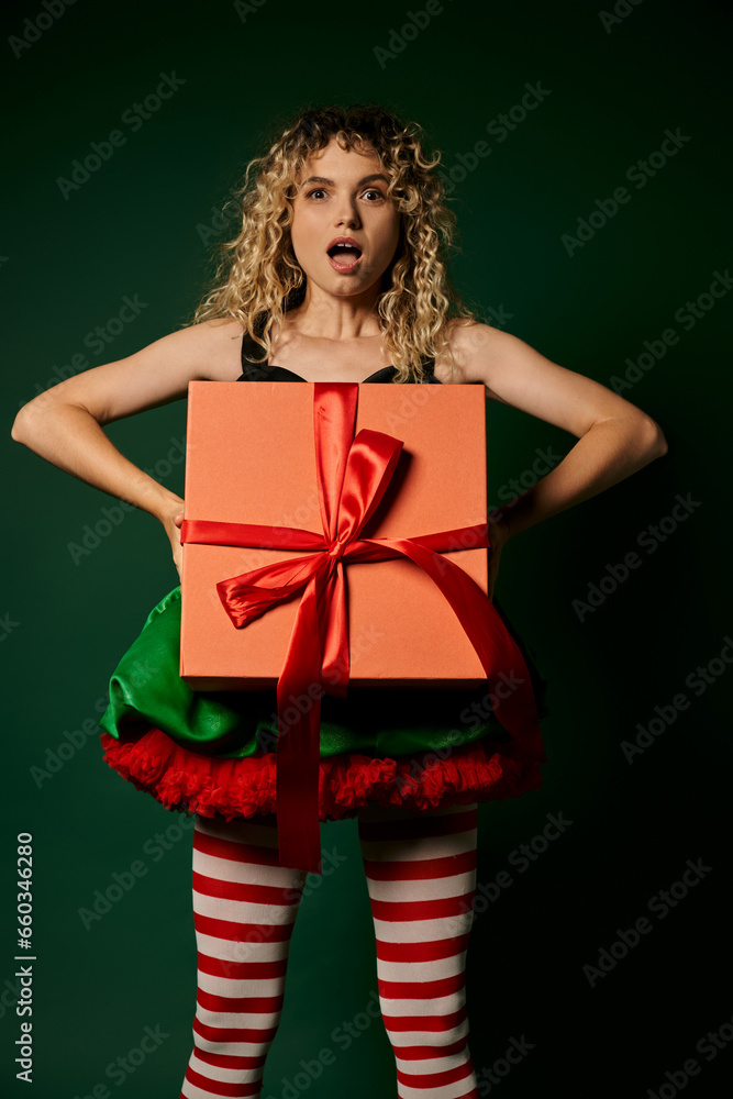 amazed woman dressed as new year elf holding present in front of her looking surprised at camera amazed woman dressed as new year elf holding present in front of her looking surprised at camera