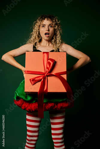 amazed woman dressed as new year elf holding present in front of her looking surprised at camera © LIGHTFIELD STUDIOS