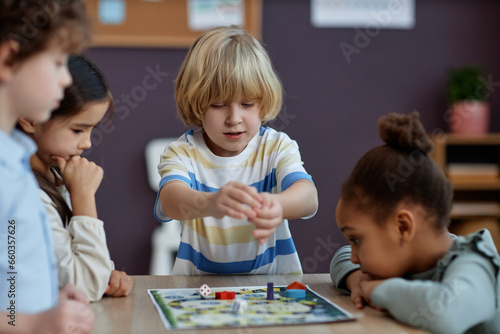 Diverse group of little kids playing board game together in preschool and throwing dice  copy space