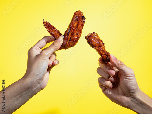 Two hands are holding pieces of grilled chicken wings isolated against a yellow background.