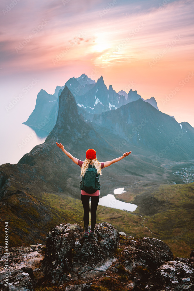 Traveler woman with backpack hiking in Norway girl raised arms alone on mountain top outdoor travel summer vacations active healthy lifestyle success motivation concept explore Senja island - obrazy, fototapety, plakaty 
