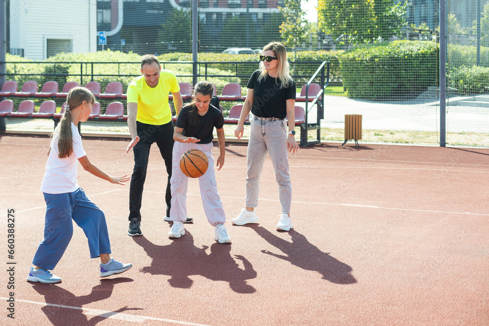 summer holidays, sport and people concept - happy family with ball playing on basketball playground