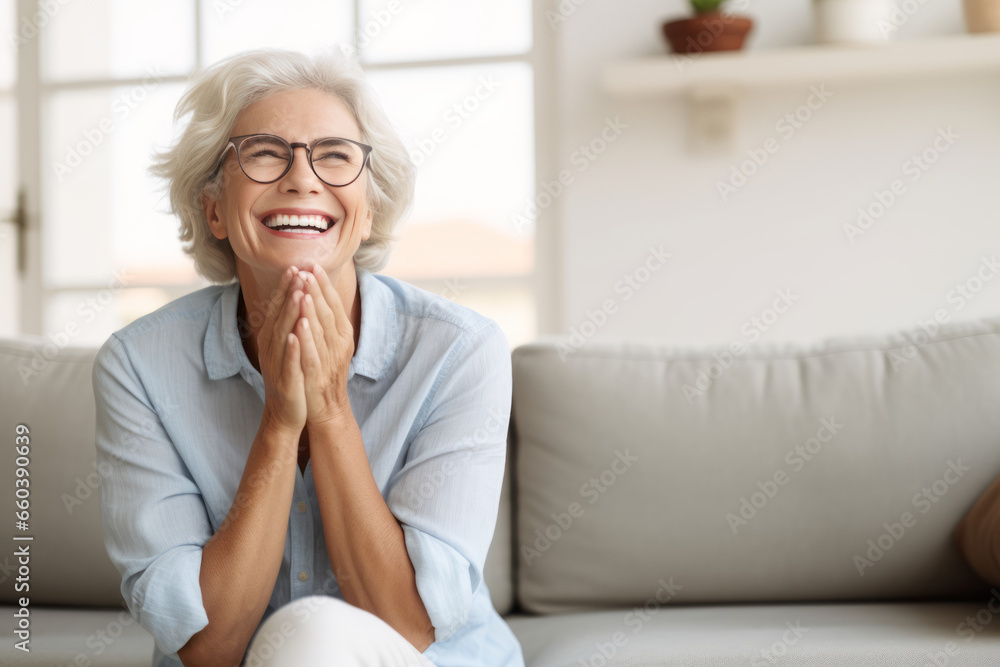 Cheerful pretty older woman in elegant glasses sitting on cozy home couch, smiling with perfect white teeth, laughing with hands at chest gesture, enjoying leisure, comfort, having fun Cheerful pretty older woman in elegant glasses sitting on cozy home couch, smiling with perfect white teeth, laughing with hands at chest gesture, enjoying leisure, comfort, having fun