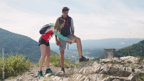 Smiling young man and a girl on a summer hiking trip, applying protection spray, a tick and mosquito repellent, with beautiful mountain scenery in the background, handheld shot. photo