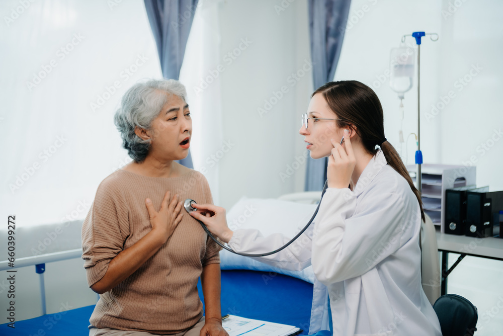 Fototapeta premium Doctor in white suit take notes while discussing and Asian elderly, woman patient who lying on bed with receiving saline solution in hospital or clinic.