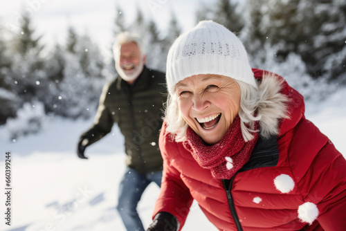 Happy mature couple in winter during snow having fun outdoors in the forest playing snowballs fight. Active healthy lifestyle in retirement photo