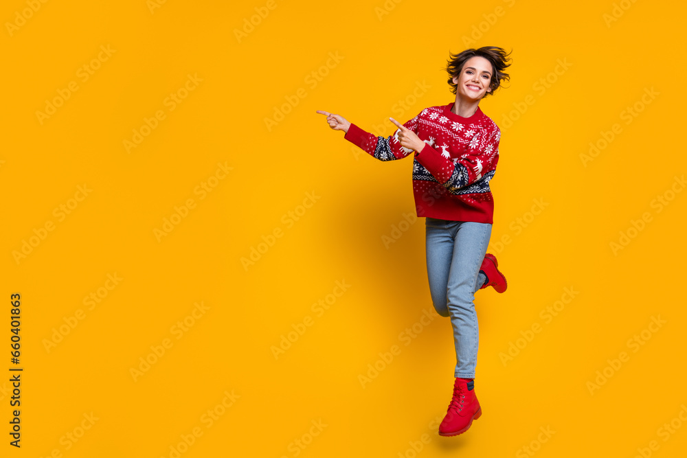 Full length photo of nice girl dressed red jumper flying indicating at christmas offer empty space isolated on yellow color background Full length photo of nice girl dressed red jumper flying indicating at christmas offer empty space isolated on yellow color background