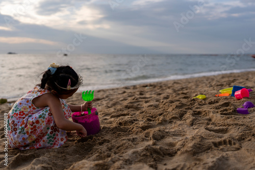 Little girl on the shore playing beach toy at dusk.