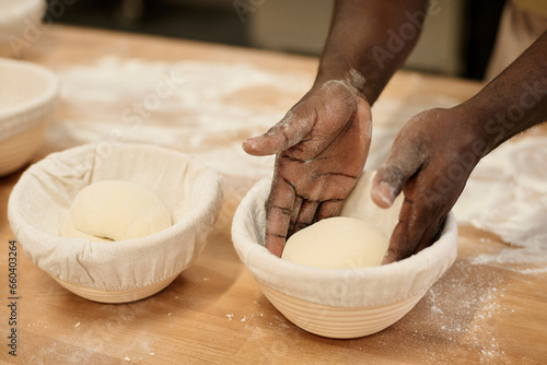 Closeup of Black young man carefully putting fresh dough in bowl at bakery kitchen, copy space