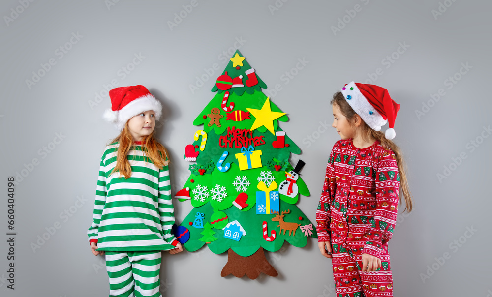 Φωτογραφία Two little girls in pajamas decorating wall of the room by green toy fir Christmas tree