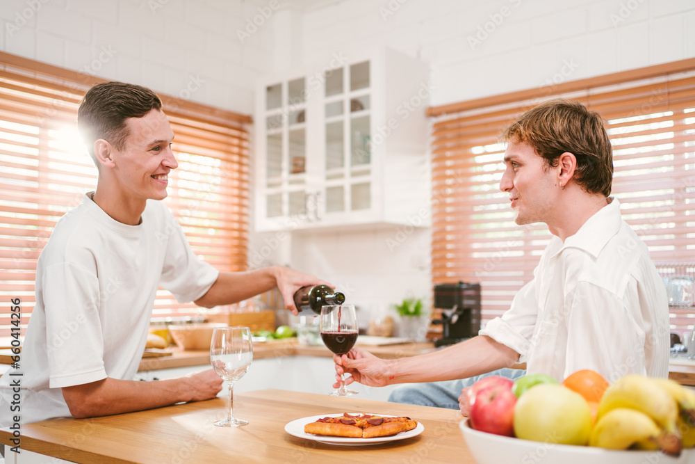 Caucasian gay attractive couple pouring and drinking red wine together in the home kitchen with fun and smiling. Homosexuality, same-sex relationships, LGBT, gay partner and romance concept. Caucasian gay attractive couple pouring and drinking red wine together in the home kitchen with fun and smiling. Homosexuality, same-sex relationships, LGBT, gay partner and romance concept.