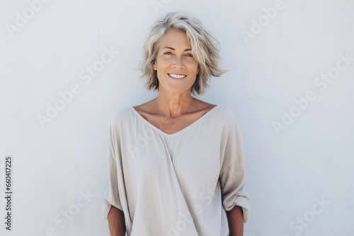 Smiling 60 year old woman standing in front of an outdoor wall. photo