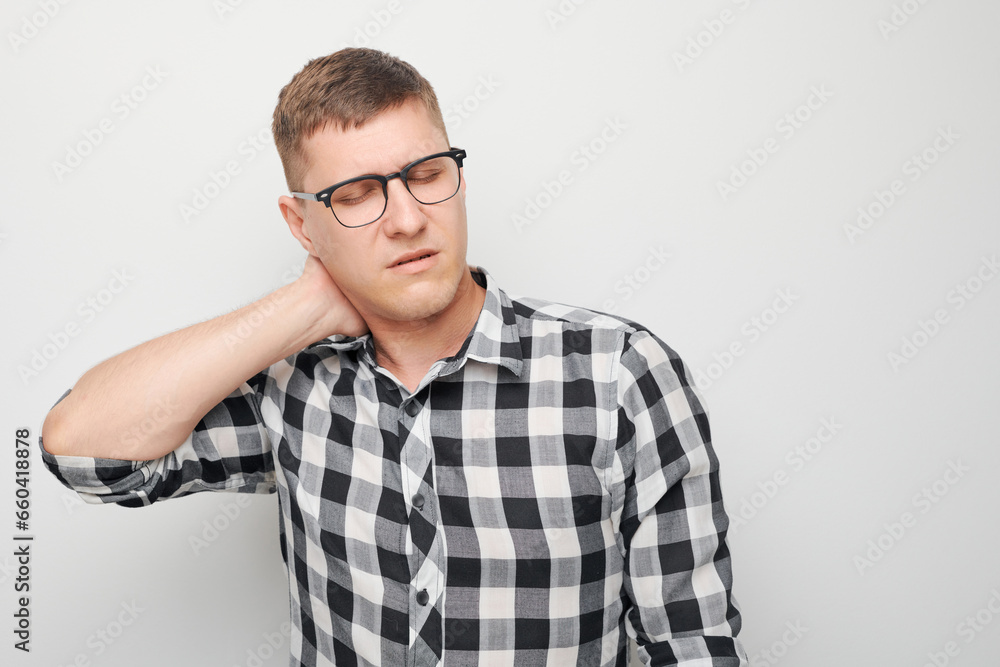 Portrait of young man suffering from pain, touching neck isolated on white studio background. Psychosomatics of stress, degenerative disease of spine Portrait of young man suffering from pain, touching neck isolated on white studio background. Psychosomatics of stress, degenerative disease of spine