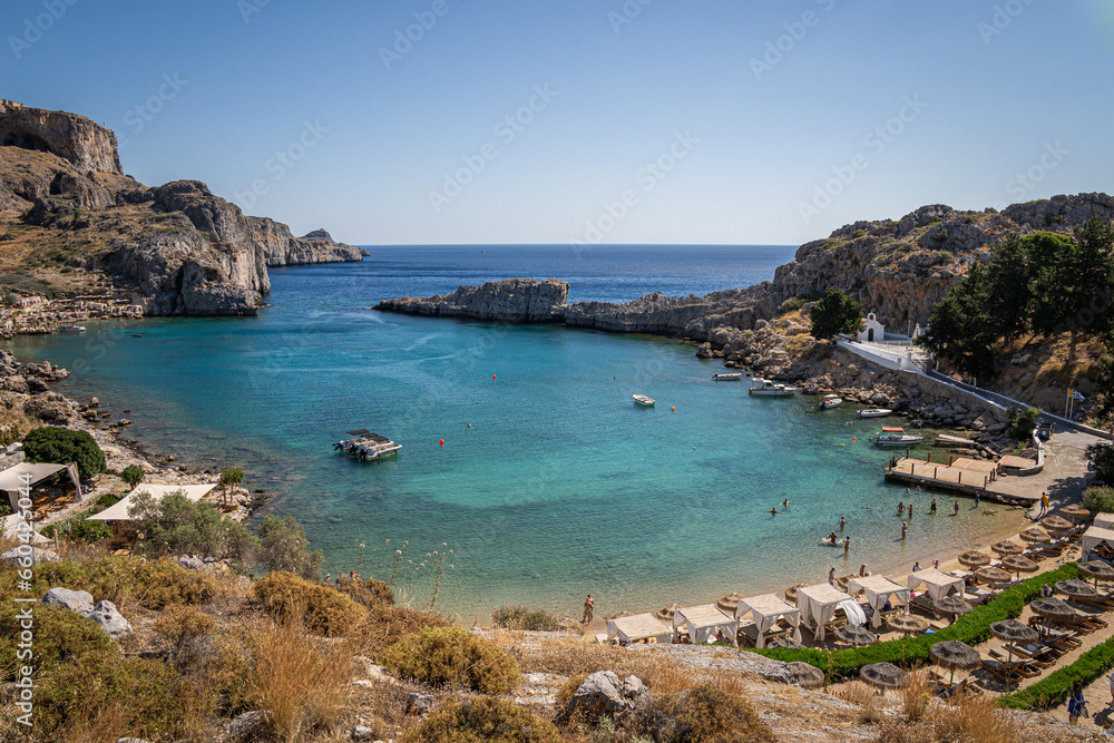 Picturesque Bay in Lindos, Rhodes: A serene sanctuary where a beautiful beach, moored boats, and the captivating turquoise embrace of the Mediterranean converge.