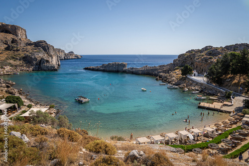 Picturesque Bay in Lindos, Rhodes: A serene sanctuary where a beautiful beach, moored boats, and the captivating turquoise embrace of the Mediterranean converge.