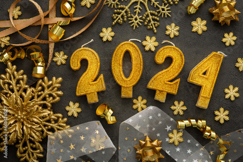 Merry Christmas and Happy New Year 2024, 2024 cake candles and various holiday decorations and ribbons in gold color on black background © pundapanda
