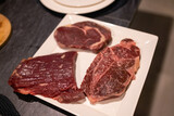 A large and delicious grilled beef steak is a great way to taste meat and freshly prepared homemade dishes. In the photo there are three large pieces of raw meat in a white plate, a frame from above.