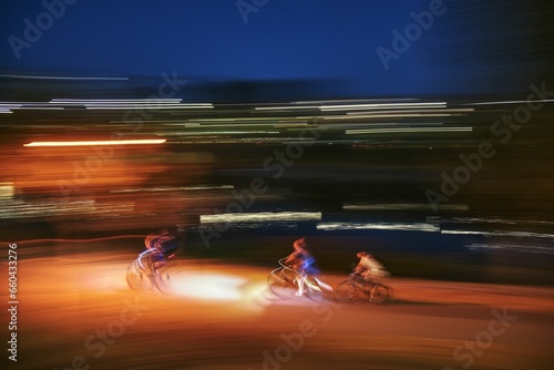 Long exposure of three silhouetted bikers, illuminated by a streetlight