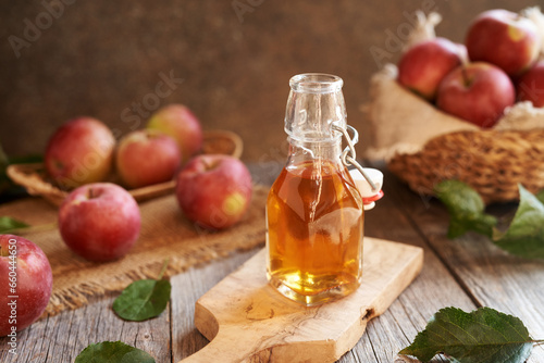 Apple cider vinegar in a glass bottle, with red apples