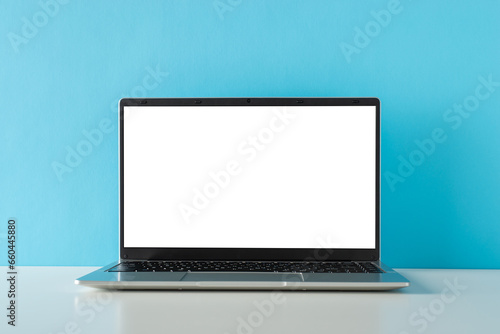 Freelance work in focus. Side view photo of contemporary laptop graces a minimalist tabletop against a blue wall backdrop, offering space for your text or advertizing