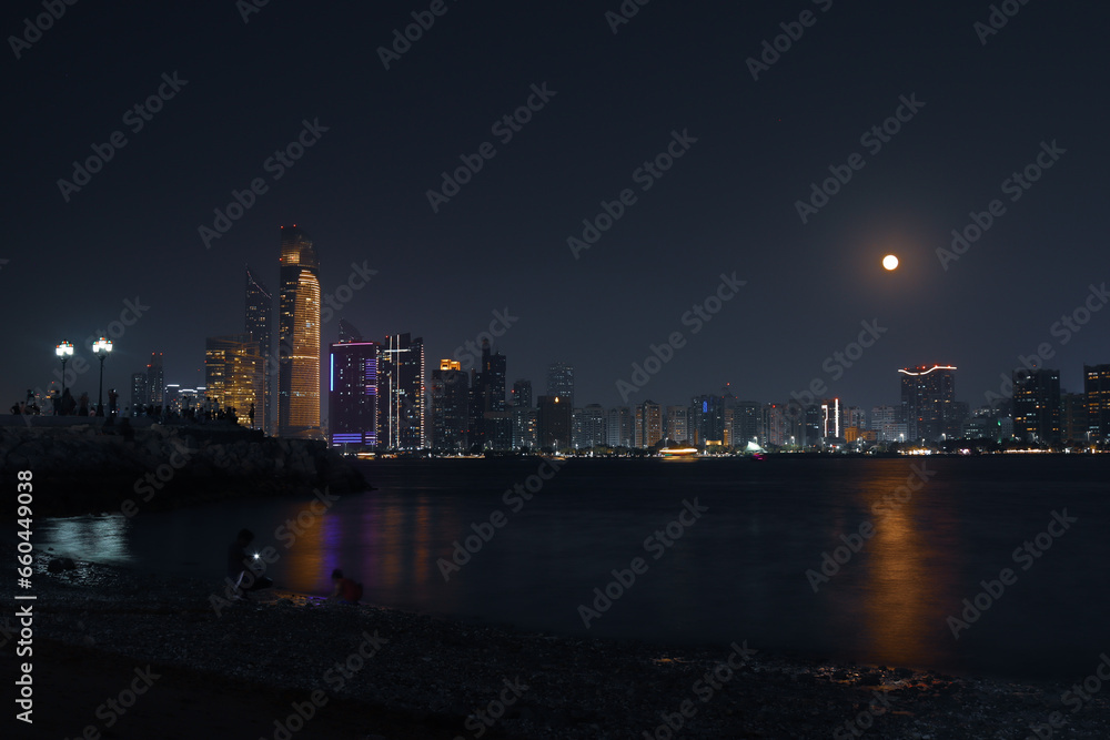 Abu dhabi city skyline at night and rise of full moon