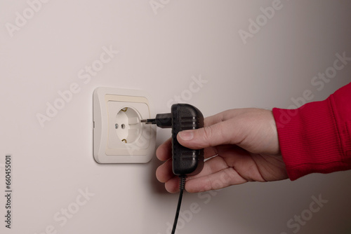 Man hand inserts an electrical plug into outlet closeup