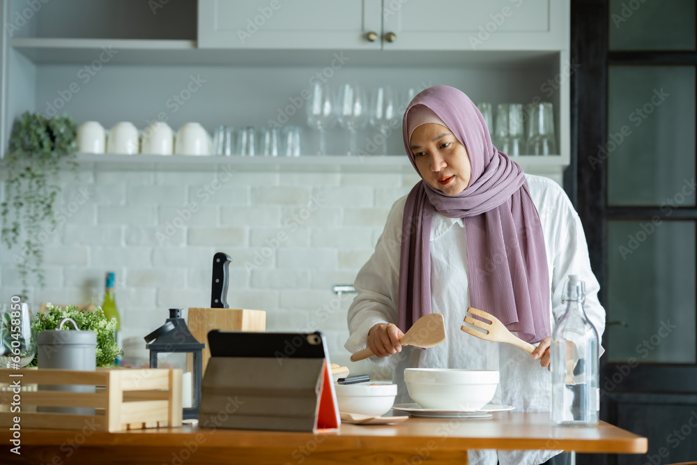 muslim mother looking at recipe from laptop and cooking. having fun woman with hijab preparing dinner, Islamic woman Enjoying Doing Homemade, Teaching cooking online muslim mother looking at recipe from laptop and cooking. having fun woman with hijab preparing dinner, Islamic woman Enjoying Doing Homemade, Teaching cooking online