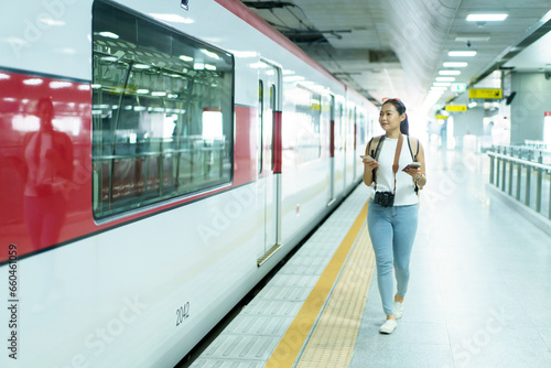 Happy beautiful Asian woman waiting for a train at railway platform. Lonely Asian female tourist or traveler standing at train station.